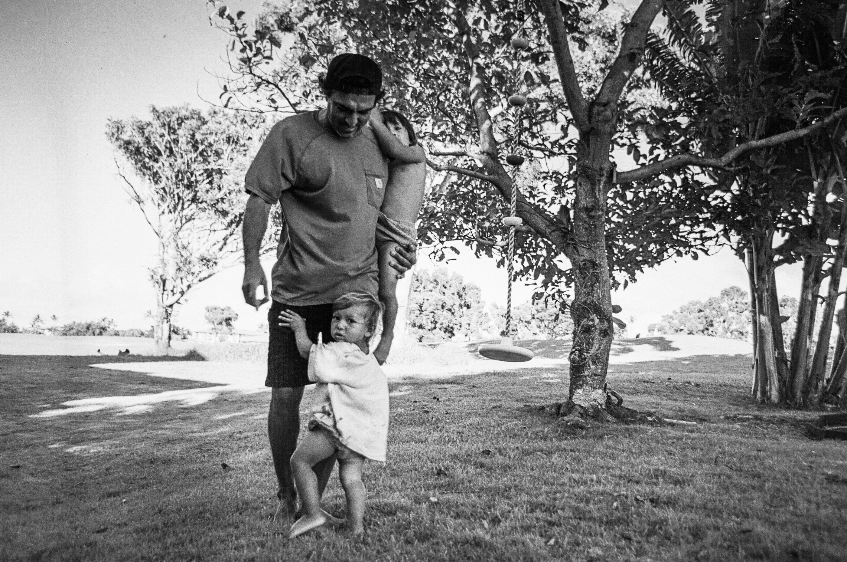 A father walking beneath a tree with two children in black and white