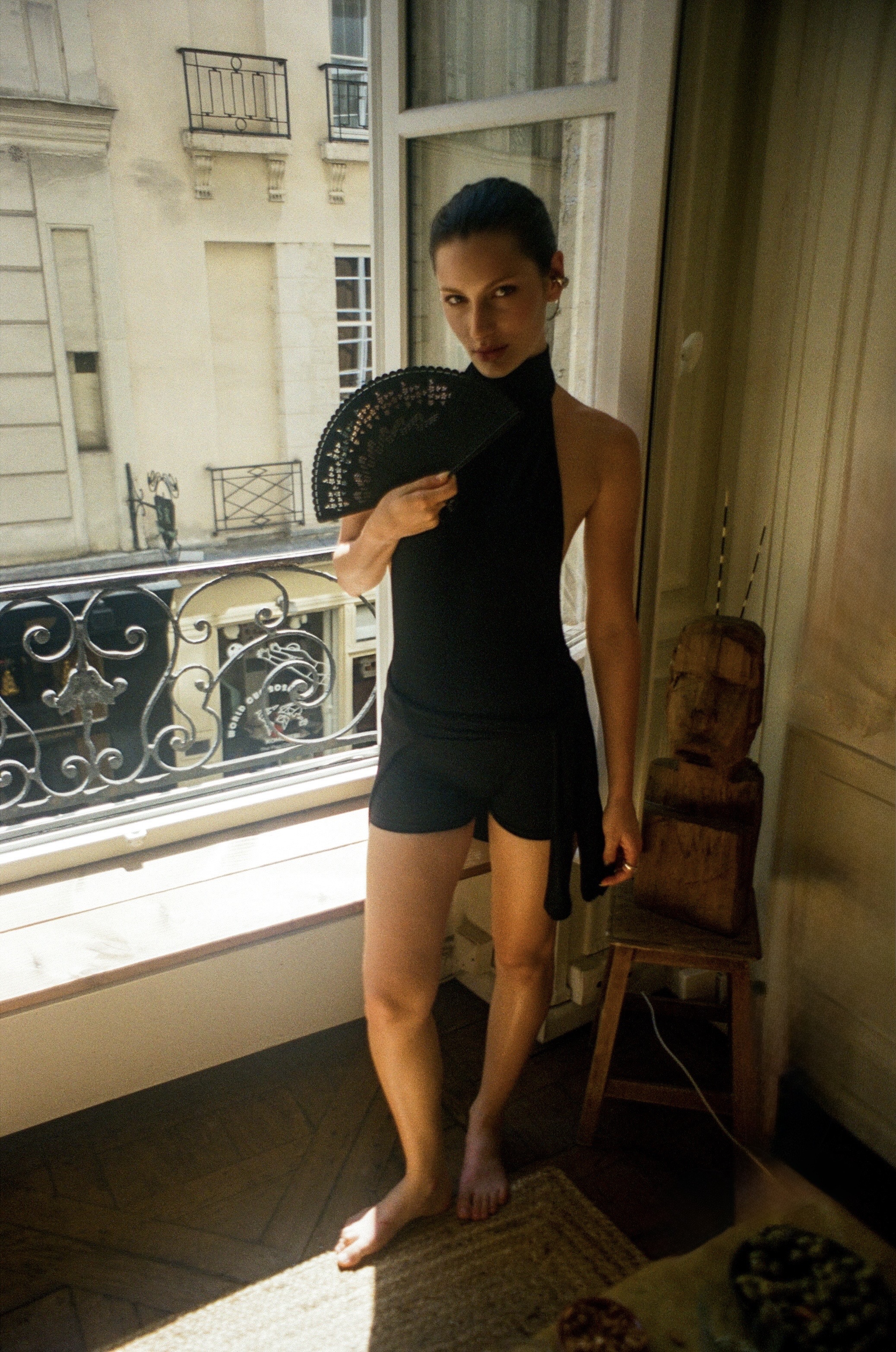 Fashion portrait in black holding a fan by a window